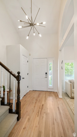 11128 South Barrett Pk Circle Sandy, UT 84092 - Photo 3 of 36 Grand foyer featuring a vaulted ceiling with a modern sputnik chandelier, light wood-finish flooring, a white paneled entry door with sidelight, and a carpeted staircase with dark wood newel post and white balusters