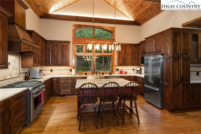 a kitchen with stainless steel appliances granite countertop a stove top oven a refrigerator a sink and a dining table with wooden cabinets