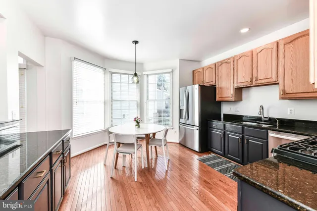 a kitchen with stainless steel appliances granite countertop a stove top oven a sink dishwasher a dining table and chairs with wooden floor