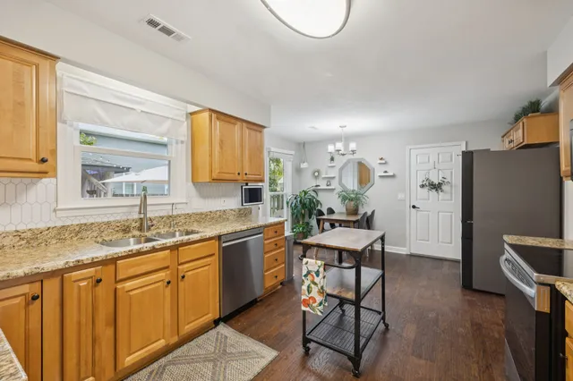 a kitchen with stainless steel appliances granite countertop a stove top oven a sink dishwasher a dining table and chairs with wooden floor