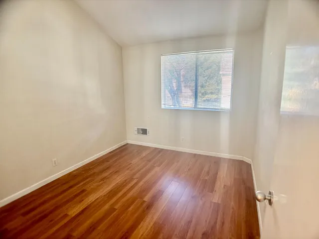 a view of an empty room with wooden floor and a window