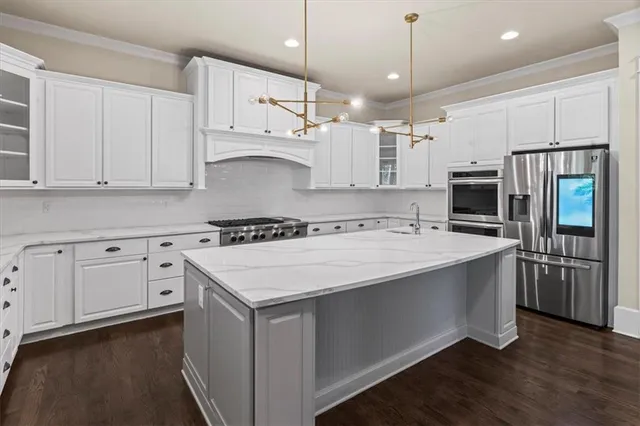 a kitchen with stainless steel appliances granite countertop a white stove top oven a refrigerator a oven and white cabinets with wooden floor