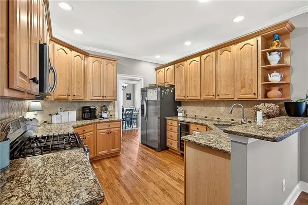 a kitchen with stainless steel appliances granite countertop a stove top oven a refrigerator a sink and dishwasher with wooden floor