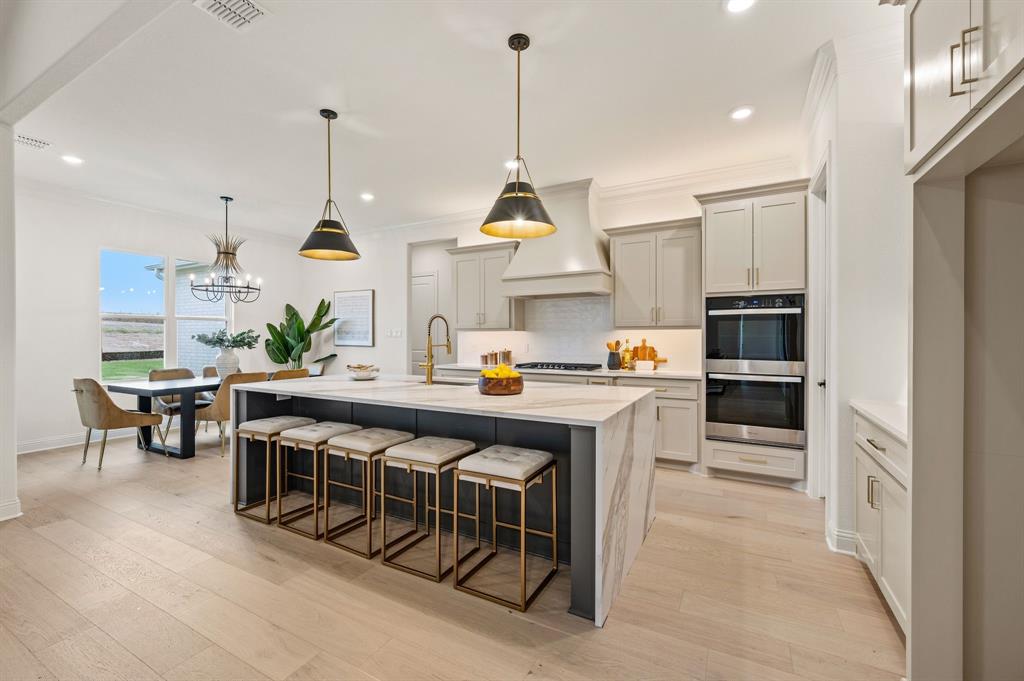 3006 Wheeler Branch Road Granbury, TX 76049 - Photo 11 of 29 Contemporary kitchen featuring a large central island with waterfall countertop, light wood-finish flooring, light gray cabinetry, and built-in double ovens