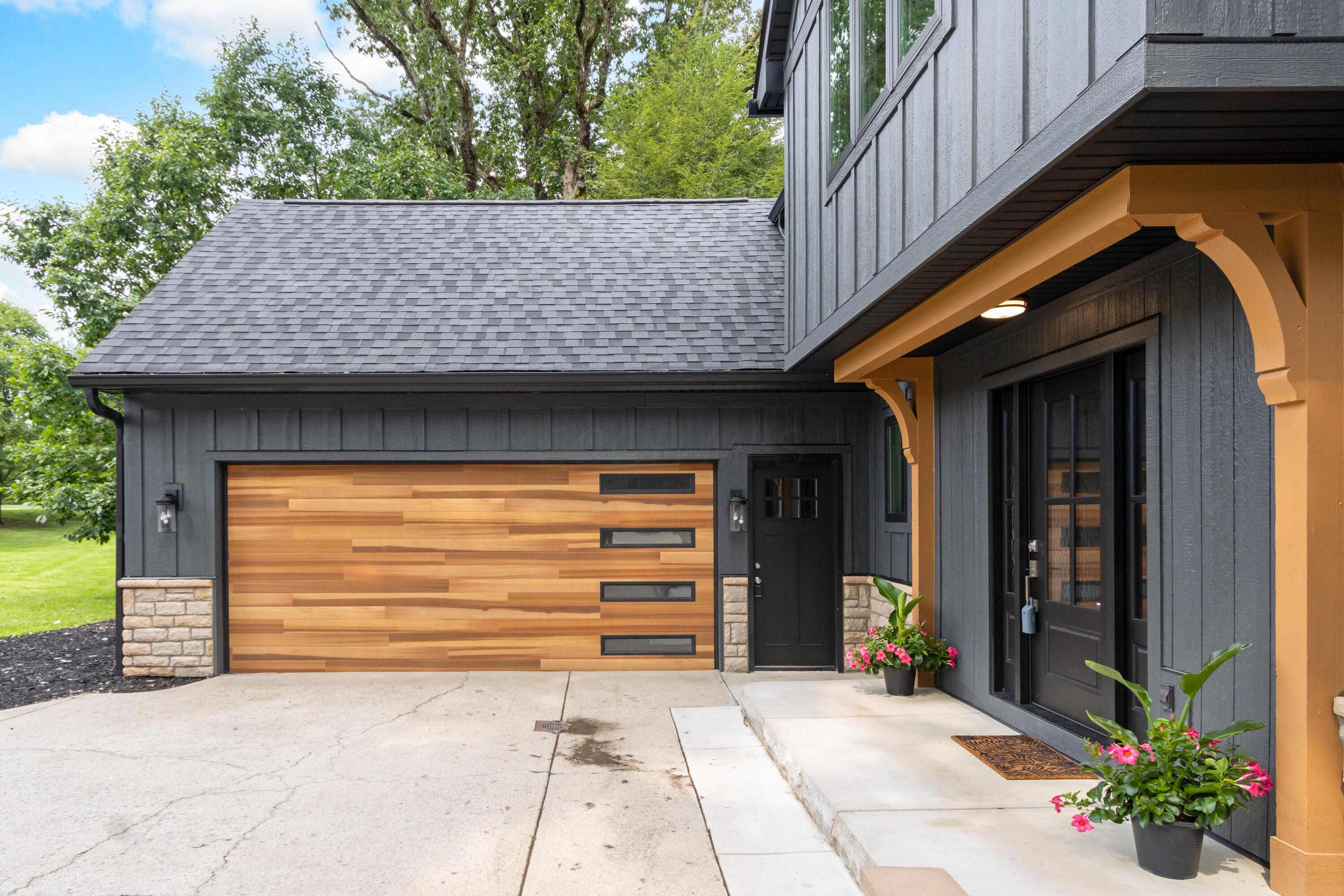1560 Carriage Road Powell, OH 43065 - Photo 7 of 73 Board and batten siding with stone accents, wood-finish garage door with horizontal windows, dark-paneled front door, and a concrete driveway