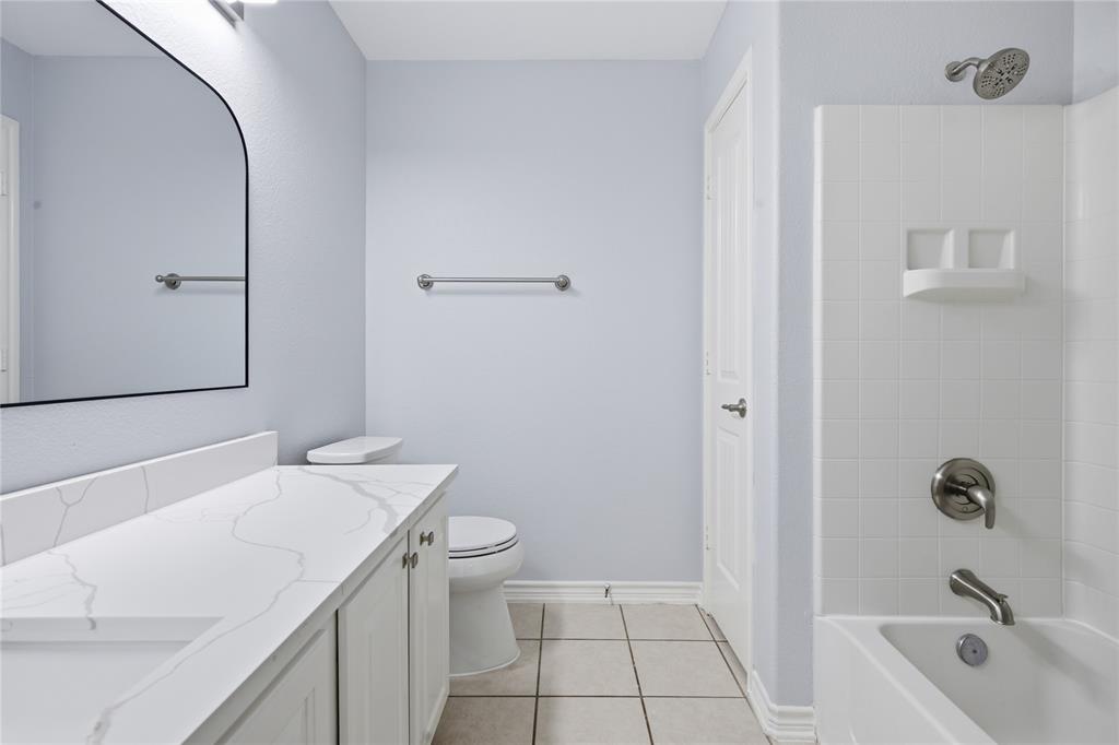 10001 Thurman Road Fort Worth, TX 76244 - Photo 25 of 40 Bathroom featuring a white vanity with a white countertop, an arched mirror, a toilet, a shower-tub combination with white subway tile surround, and light-toned tile flooring