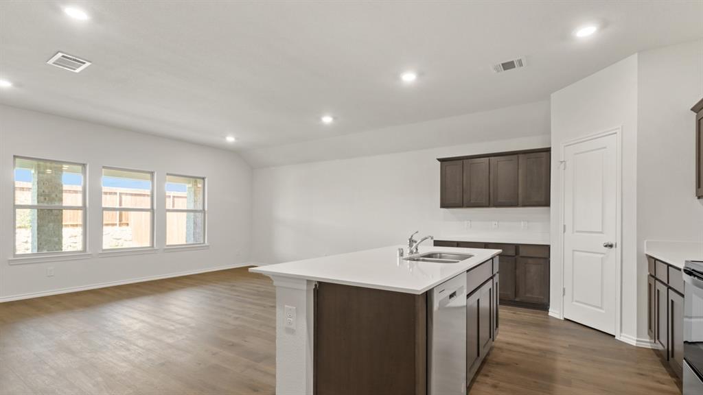 1913 Reveille Way Terrell, TX 75160 - Photo 24 of 27 Kitchen featuring a kitchen island with sink, stainless steel appliances, open floor plan, dark wood-style flooring, and light stone countertops