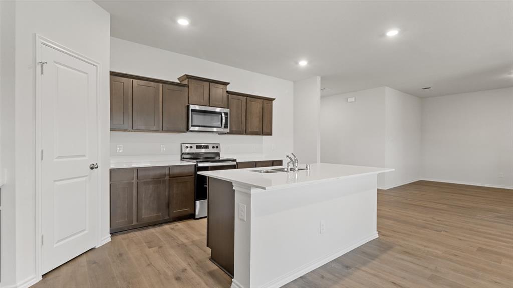 1913 Reveille Way Terrell, TX 75160 - Photo 6 of 27 Kitchen featuring stainless steel appliances, dark wood finish cabinetry, an island with sink, light wood finished floors, and recessed lighting
