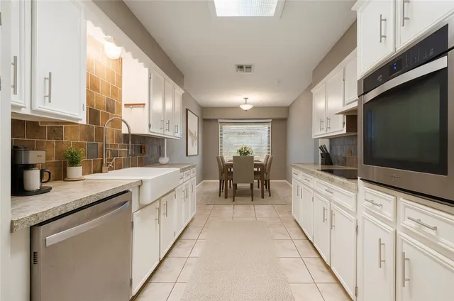 a large white kitchen with granite countertop a sink and dishwasher a stove top oven with wooden floor