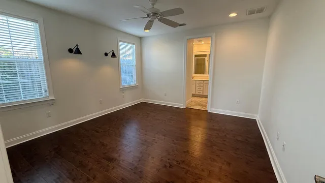 an empty room with wooden floor chandelier fan and windows