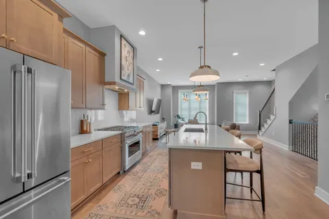 a large kitchen with stainless steel appliances granite countertop a refrigerator a oven a sink and a dining table with wooden floor