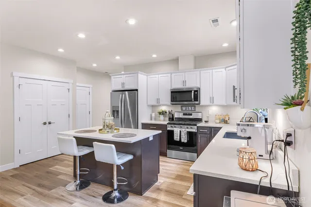 a kitchen with stainless steel appliances kitchen island granite countertop a sink dishwasher a stove a refrigerator a microwave oven with white cabinets and wooden floor