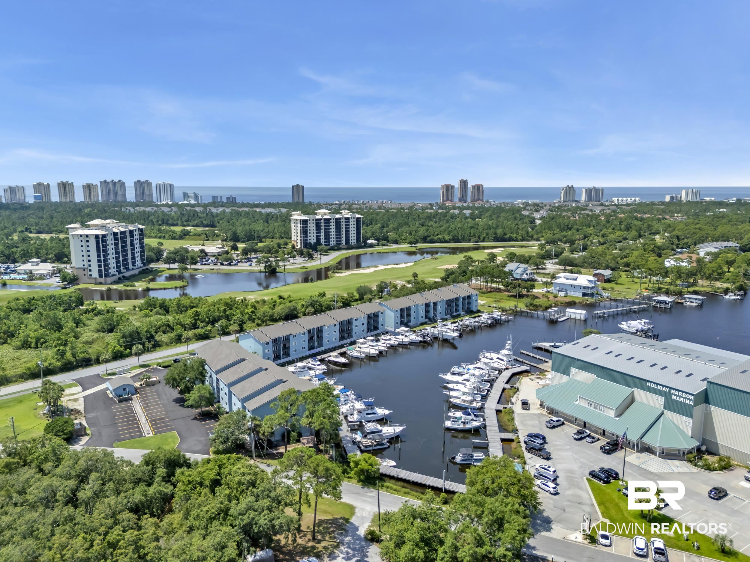 14100 River Road, Unit 211 Pensacola, FL 32507 - Photo 54 of 56 Marina with multiple boat slips, surrounded by lush green landscaping, golf course, and distant coastal architecture
