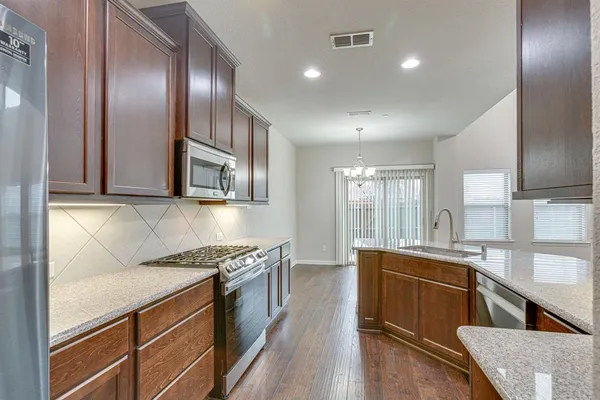 a kitchen with stainless steel appliances granite countertop a stove top oven a sink dishwasher and a refrigerator with wooden floor