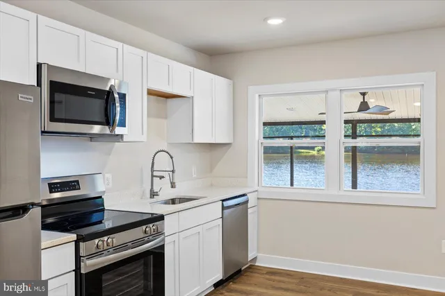 a kitchen with stainless steel appliances granite countertop a stove a refrigerator a sink a microwave oven with white cabinets and wooden floor