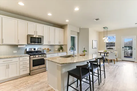a kitchen with stainless steel appliances granite countertop a stove a sink a microwave a dining table and chairs