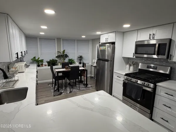 a kitchen with stainless steel appliances kitchen island granite countertop a refrigerator a stove a sink a dining table and chairs with wooden floor