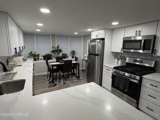 a kitchen with stainless steel appliances kitchen island granite countertop a refrigerator a stove a sink a dining table and chairs with wooden floor