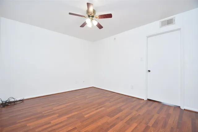 an empty room with wooden floor a ceiling fan and windows
