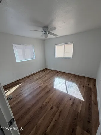 an empty room with wooden floor ceiling fan and windows