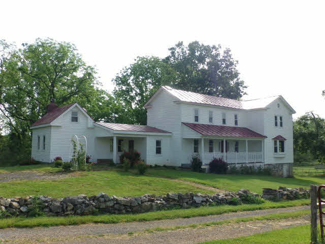 a view of a white house next to a yard with big trees