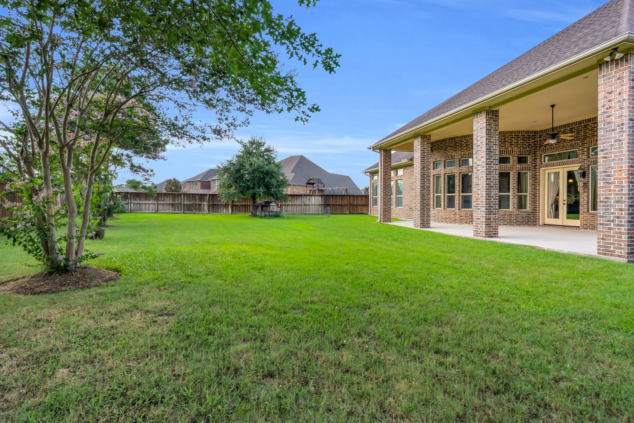 4022 Sabine Valley Trail Spring, TX 77386 - Photo 35 of 46 Spacious backyard with lush green lawn, bordered by a wooden fence for privacy. Features a covered patio with brick columns, perfect for outdoor gatherings.