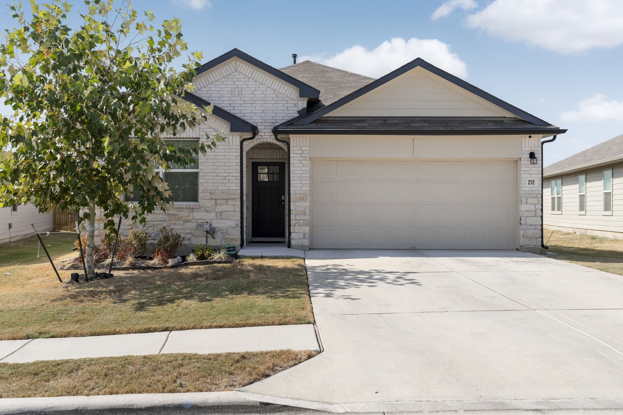 212 Apache Plum Drive Kyle, TX 78640 - Photo 1 of 21 View of front facade featuring stone siding, a garage, driveway, and a front yard