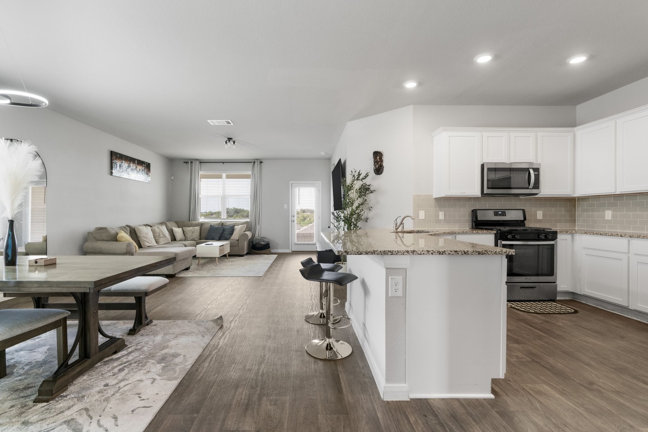 212 Apache Plum Drive Kyle, TX 78640 - Photo 6 of 21 Kitchen with stainless steel appliances, white cabinetry, a breakfast bar, light stone countertops, and backsplash