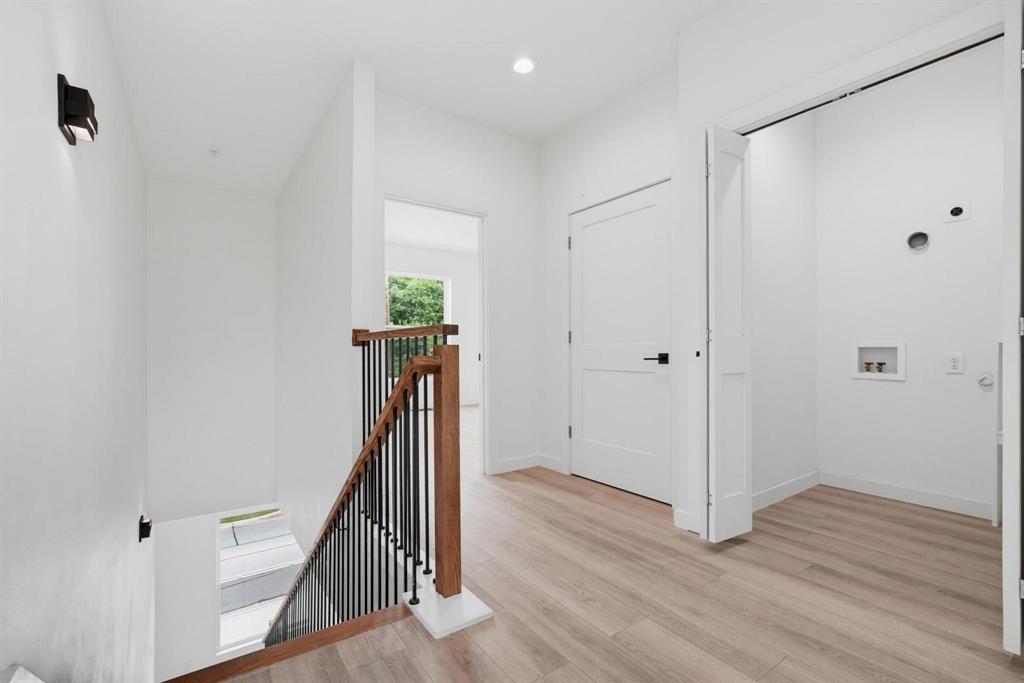 510 South O Connor Road Irving, TX 75060 - Photo 10 of 22 Bright hallway featuring wood-finish flooring, a contemporary staircase with dark metal balusters and wood handrails, recessed ceiling lighting, and a dedicated laundry area with utility hookups