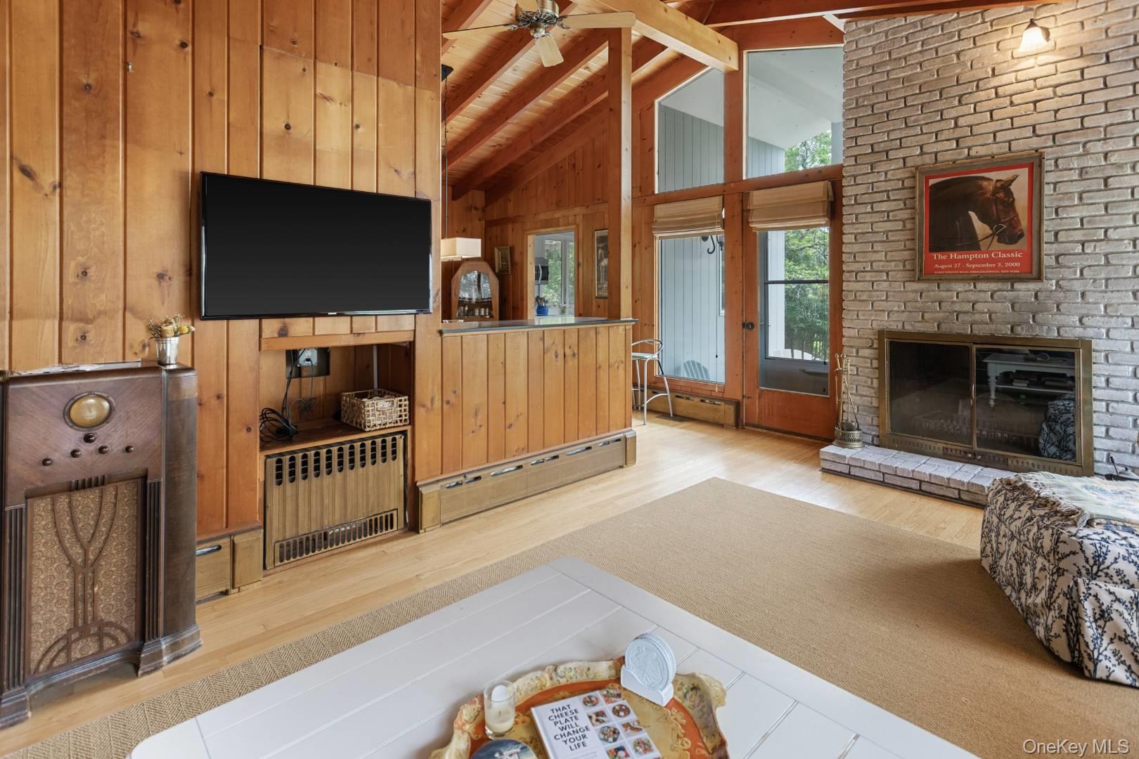 16 South Beach Road Southampton, NY 11968 - Photo 5 of 14 Living area featuring wood walls, a fireplace, a baseboard heating unit, radiator, and a ceiling fan