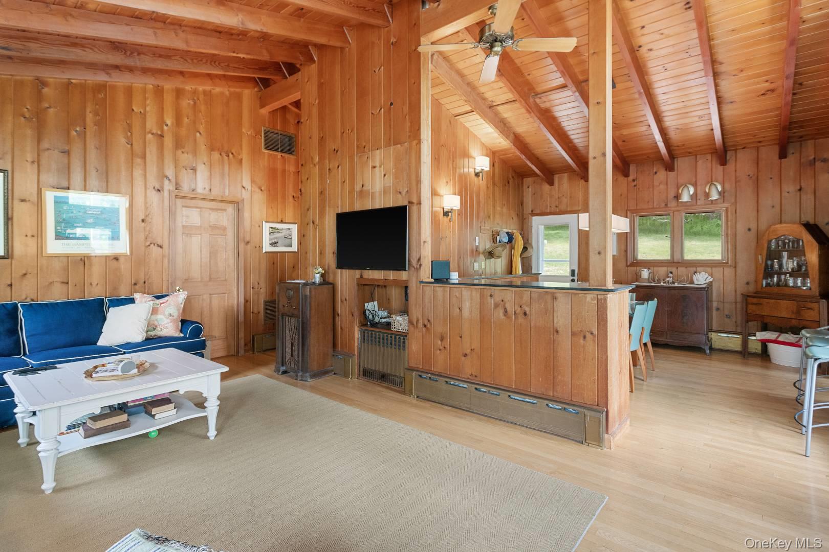 16 South Beach Road Southampton, NY 11968 - Photo 6 of 14 Living room with wood finished floors, wood walls, a baseboard radiator, high vaulted ceiling, and a wooden ceiling with exposed beams