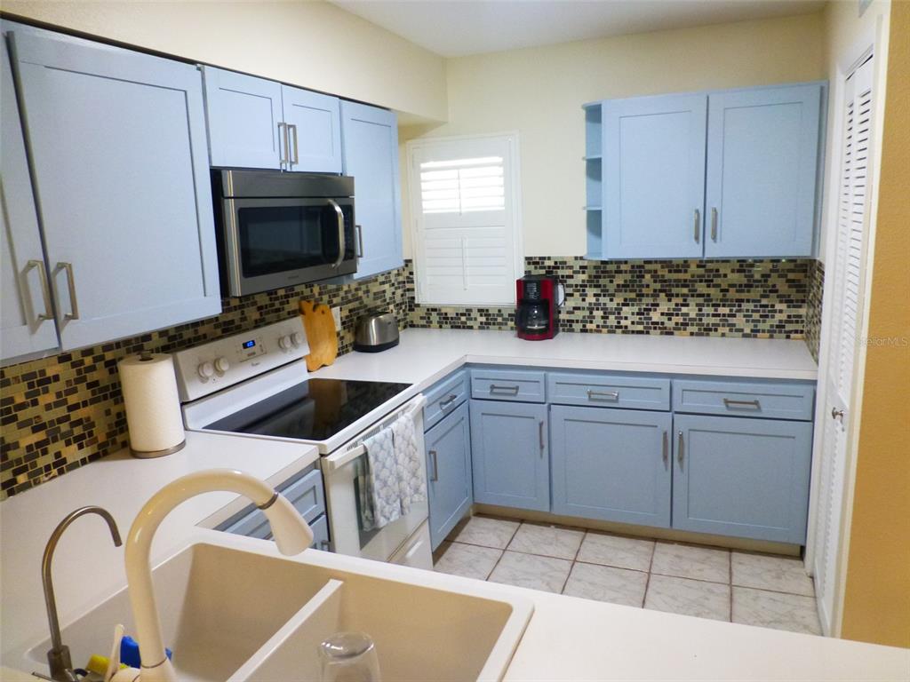 5557 Sea Forest Drive, Unit 215 New Port Richey, FL 34652 - Photo 6 of 40 a kitchen with white cabinets a sink and a stove with wooden floor