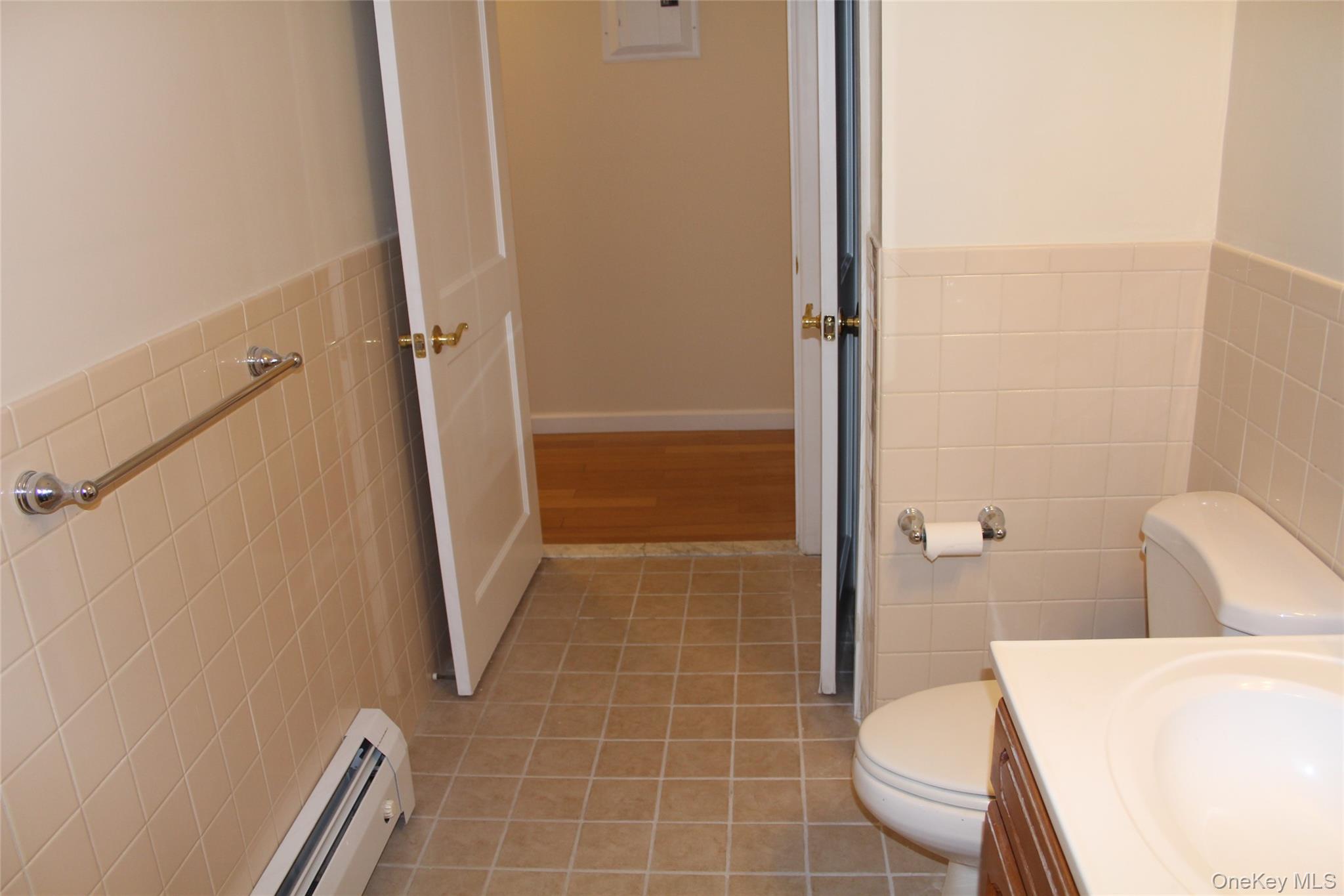 85 Bronx River Road, Unit 3S Yonkers, NY 10704 - Photo 19 of 27 Half bathroom featuring tile walls, a wainscoted wall, baseboard heating, vanity, and light tile patterned floors