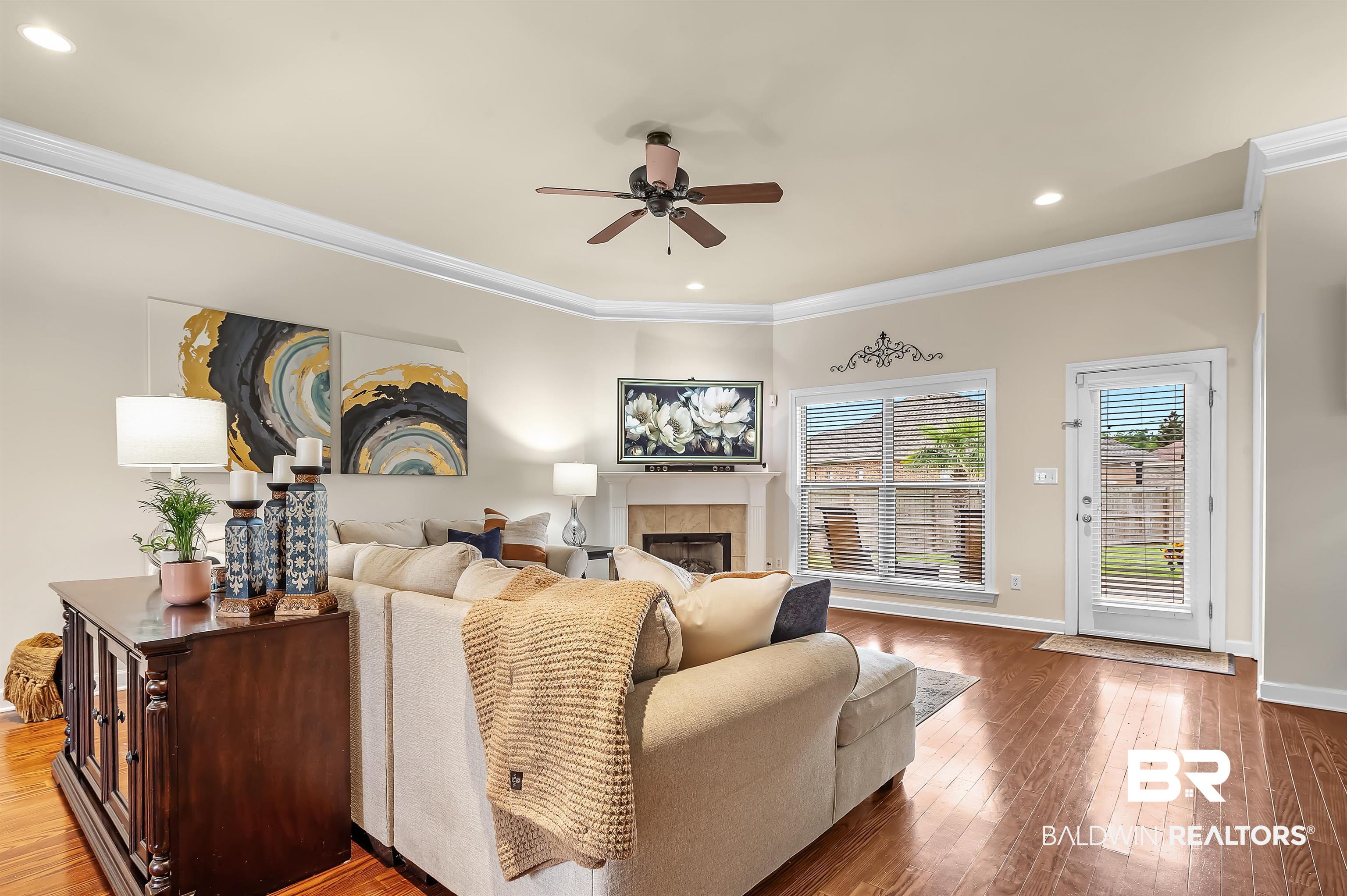 9376 Sable Court Daphne, AL 36526 - Photo 11 of 46 Living room with ornamental molding, ceiling fan, a tiled fireplace, and hardwood / wood-style floors