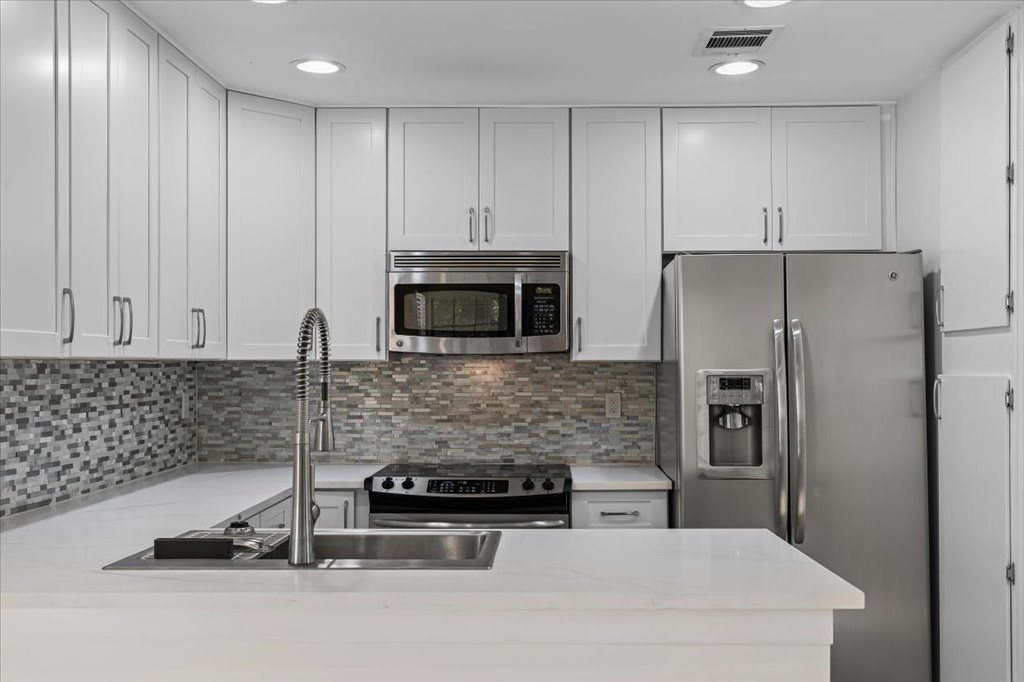 1748 Ohlen Road, Unit 75 Austin, TX 78757 - Photo 16 of 33 Kitchen with appliances with stainless steel finishes, white cabinets, backsplash, light stone countertops, and recessed lighting
