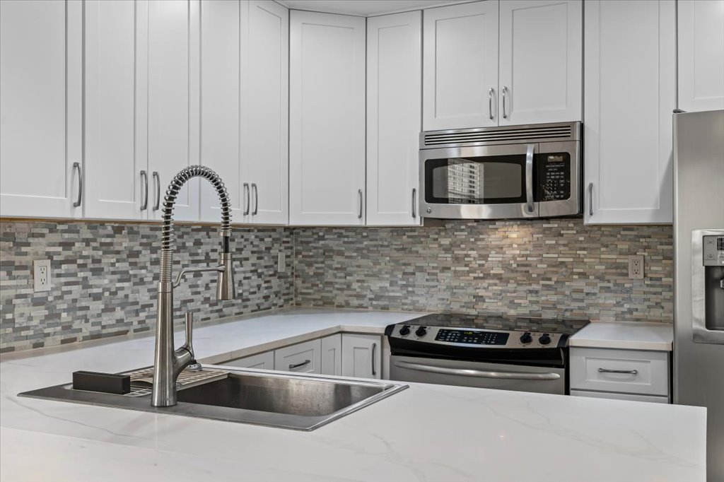 1748 Ohlen Road, Unit 75 Austin, TX 78757 - Photo 17 of 33 Kitchen with stainless steel appliances, backsplash, white cabinetry, and light stone countertops