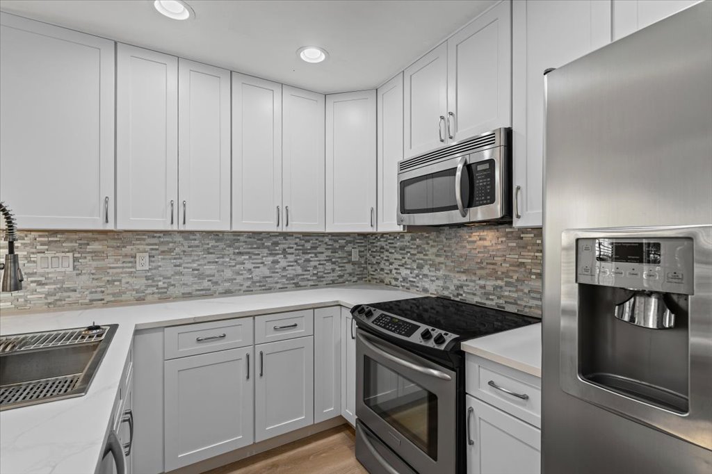 1748 Ohlen Road, Unit 75 Austin, TX 78757 - Photo 18 of 33 Kitchen with appliances with stainless steel finishes, white cabinets, backsplash, light wood-style floors, and recessed lighting