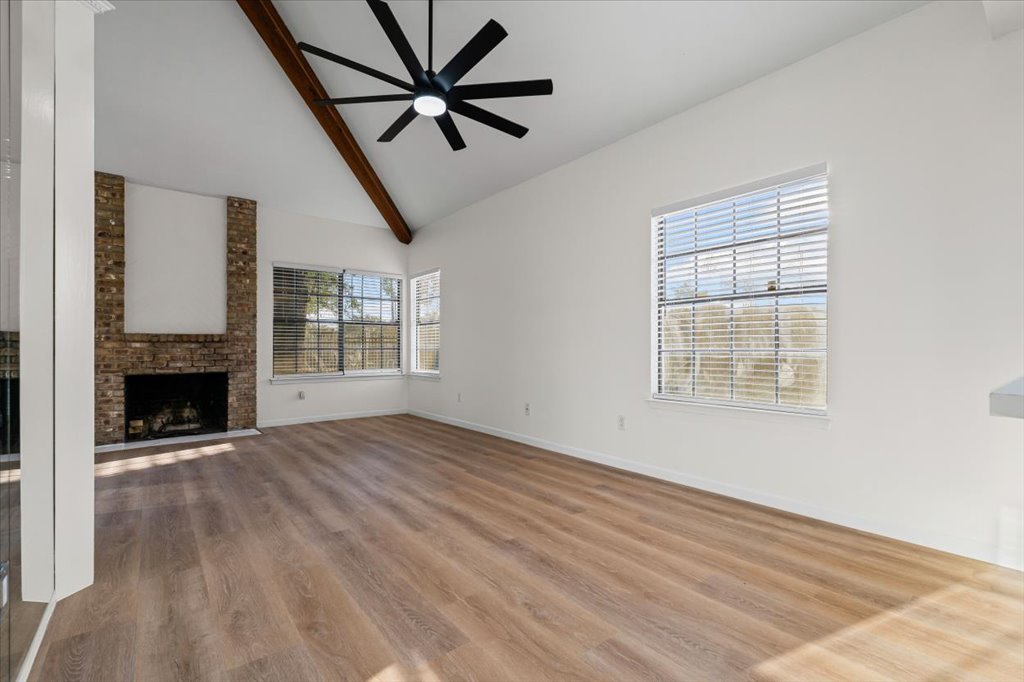 1748 Ohlen Road, Unit 75 Austin, TX 78757 - Photo 5 of 33 Unfurnished living room featuring high vaulted ceiling, beamed ceiling, a fireplace, wood finished floors, and ceiling fan