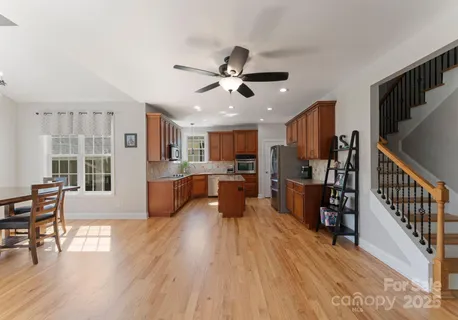 a large open kitchen with stainless steel appliances kitchen island granite countertop a refrigerator a stove a sink a dining table and chairs with wooden floor