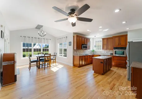 a open kitchen with stainless steel appliances granite countertop a stove top oven a refrigerator a dining table and chairs with wooden floor