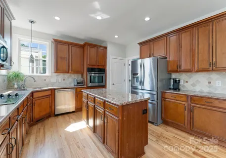 a kitchen with stainless steel appliances granite countertop a refrigerator a sink dishwasher a stove with wooden cabinets and floor