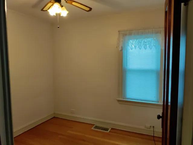 an empty room with wooden floor fan and windows