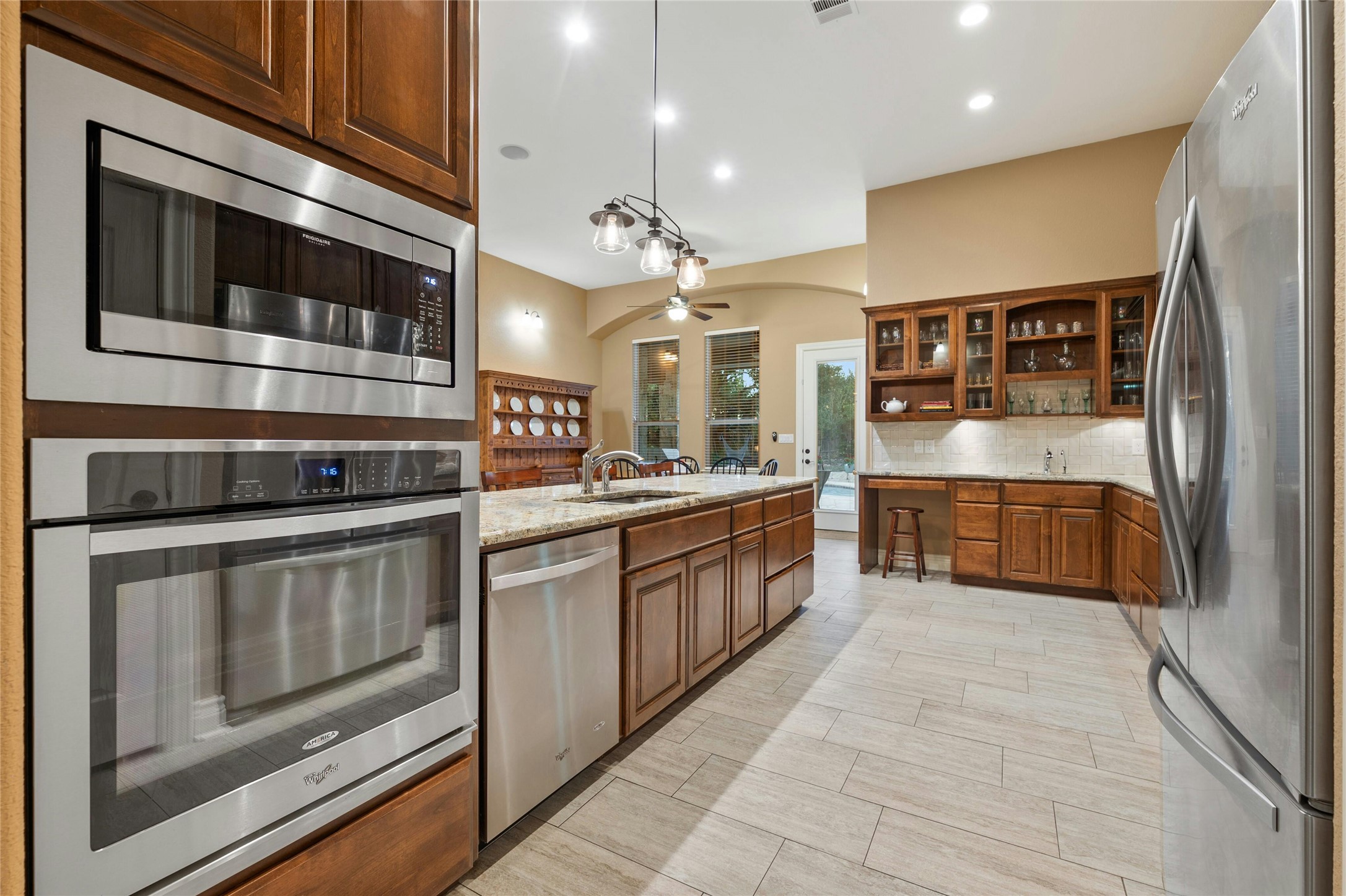 201 Greenridge Lane Dripping Springs, TX 78620 - Photo 15 of 29 Kitchen with appliances with stainless steel finishes, decorative light fixtures, light stone counters, a ceiling fan, and brown cabinetry