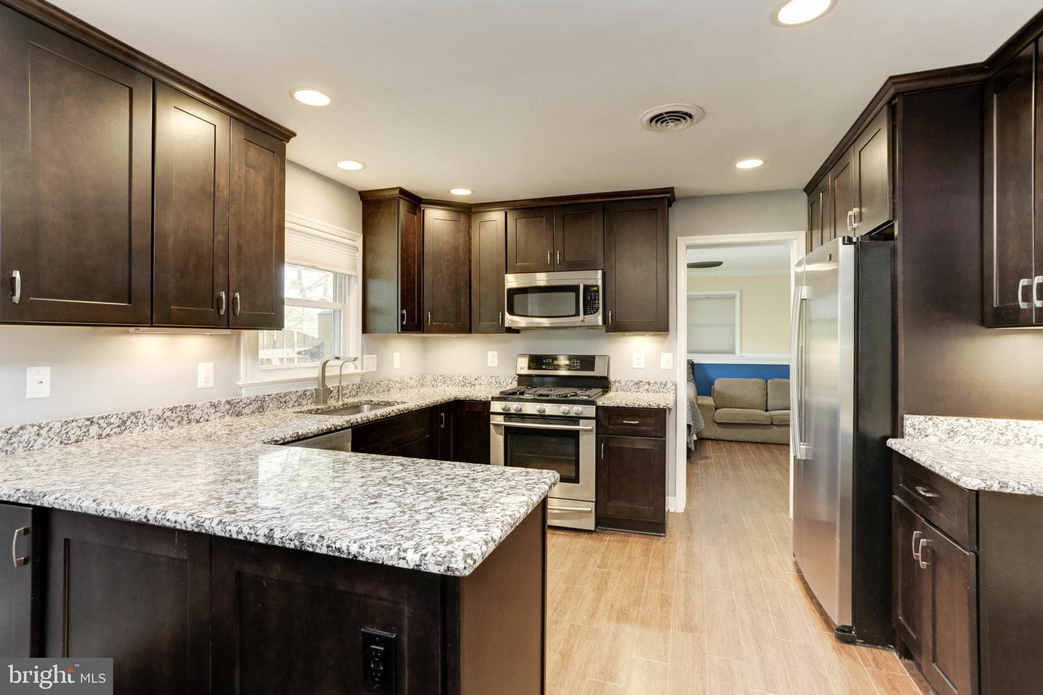 a kitchen with kitchen island granite countertop stainless steel appliances a sink stove refrigerator and cabinets