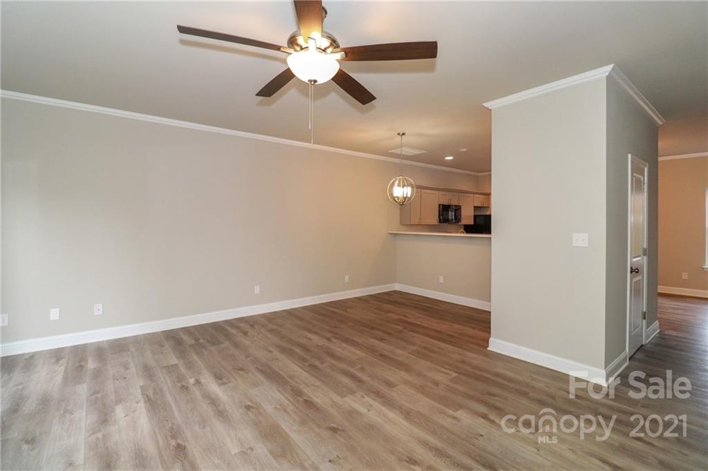 1265 Amber Ridge Road Northwest Concord, NC 28027 - Photo 12 of 26 an empty room with wooden floor a ceiling fan and kitchen view