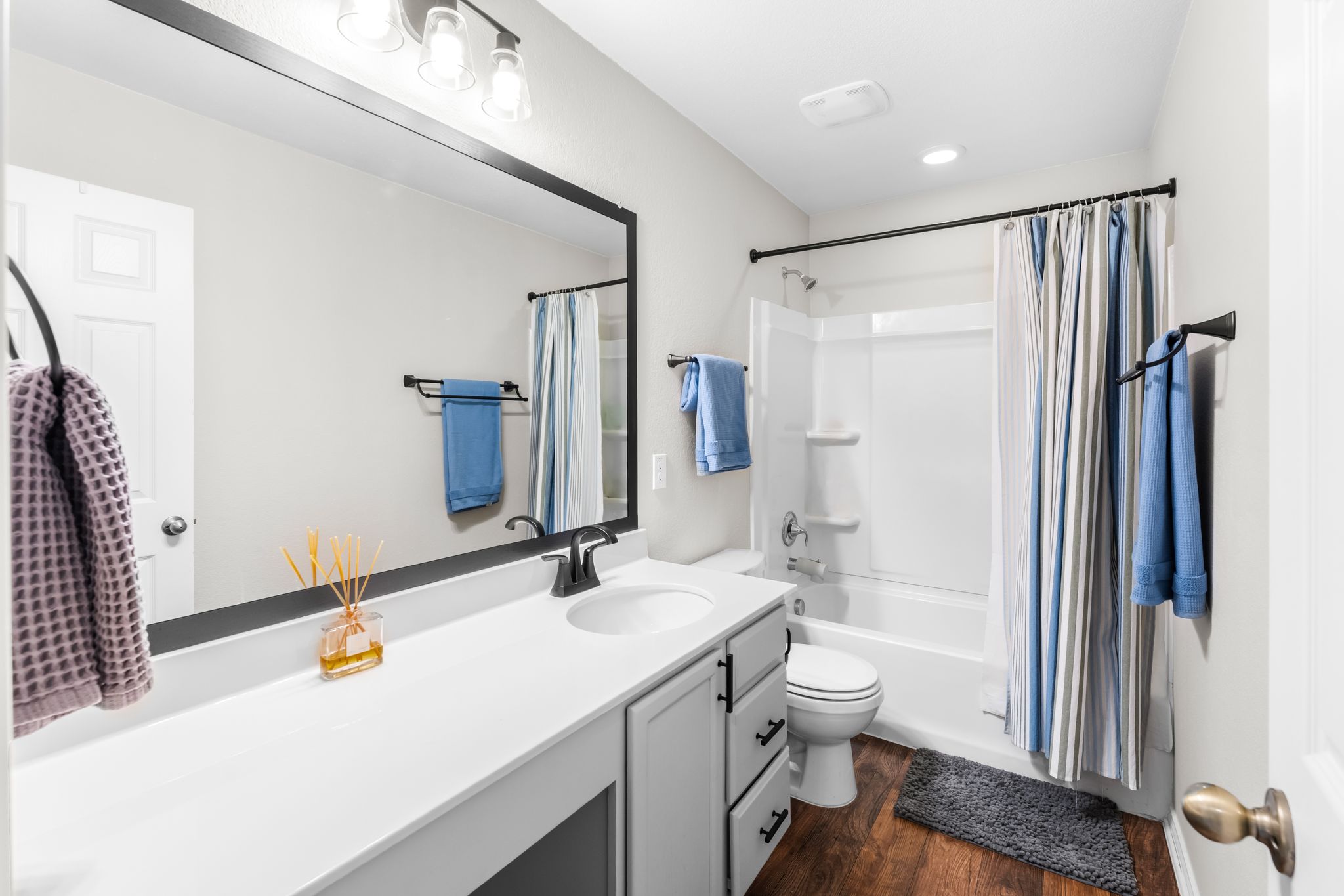 1133 Yellow Iris Road Leander, TX 78641 - Photo 27 of 37 Bathroom featuring a single vanity with a white countertop, dark wood-finish flooring, a white tub-shower combination, a wall-mounted mirror, and overhead lighting