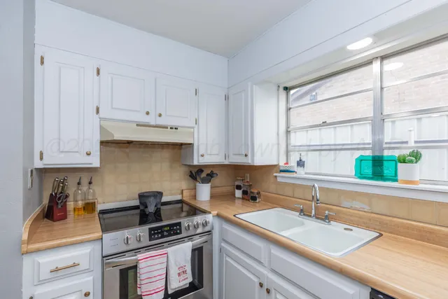 a kitchen with granite countertop a sink stainless steel appliances white cabinets and a window