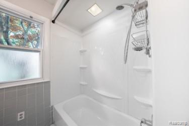 2329 Rutherford Road Bloomfield Hills, MI 48302 - Photo 42 of 46 Bathtub and shower combination with white surround, integrated shelving, and a window featuring frosted glass
