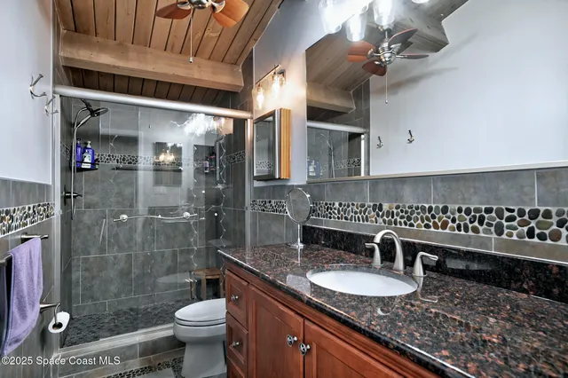 a bathroom with a granite countertop sink a toilet a mirror and shower