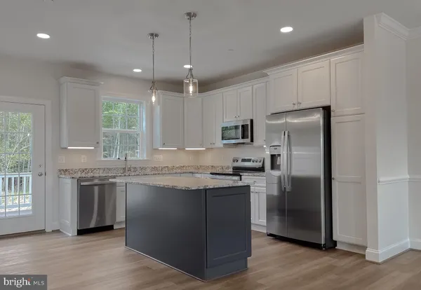 a kitchen with stainless steel appliances granite countertop a refrigerator a sink dishwasher a stove and white cabinets with wooden floor